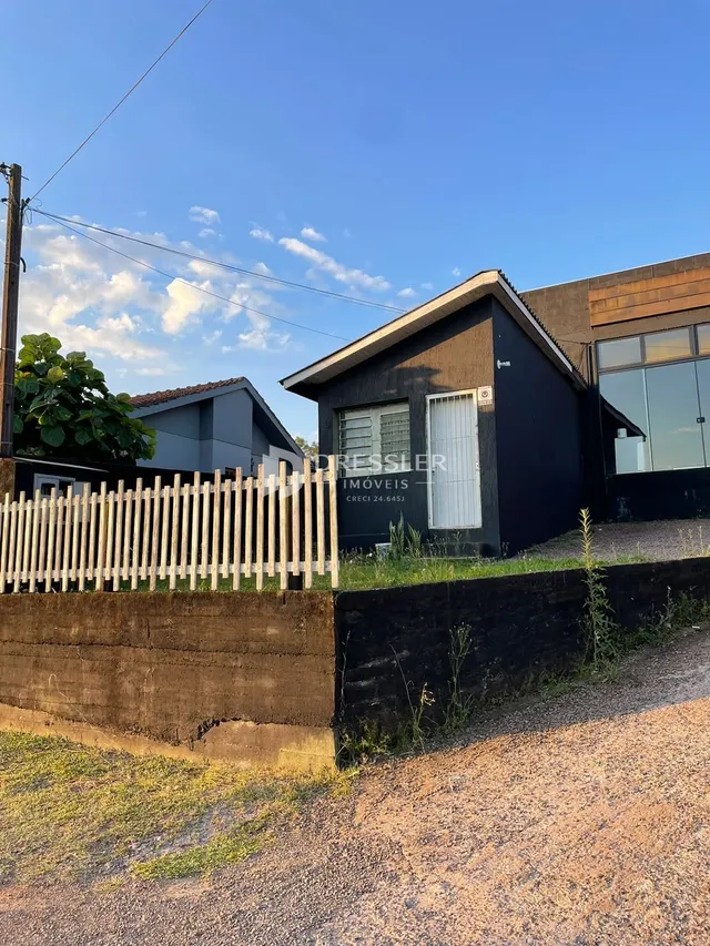 Fachada de uma casa em Lajeado, Brasil, com cerca de madeira e muro de contenção.