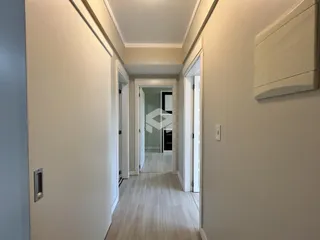Corredor interno de uma residência com piso de madeira clara.