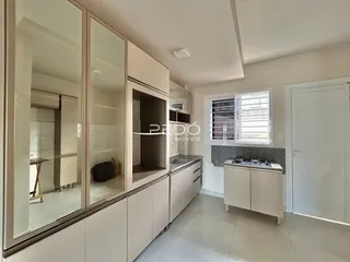 Vista interna de uma cozinha moderna com armários brancos e janela.