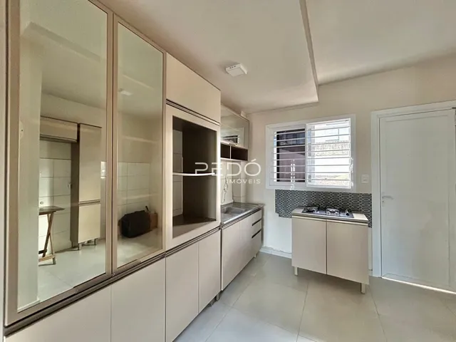 Vista interna de uma cozinha moderna com armários brancos e janela.