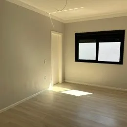 Foto de um corredor interno com piso de madeira clara e parede lisa.