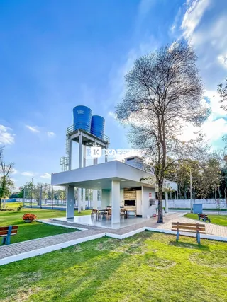 Vista externa de uma área verde com uma estrutura coberta e tanques industriais ao fundo.