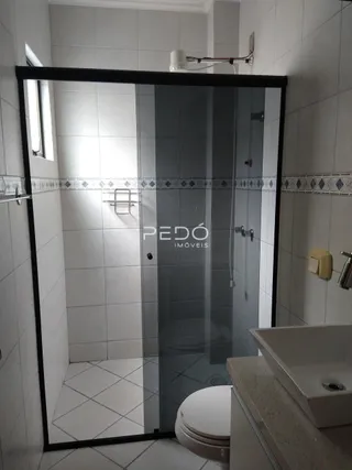 Foto de um banheiro com box de vidro e azulejos brancos.