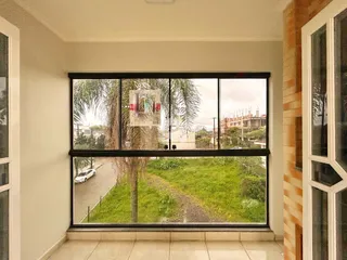 Vista externa de uma rua com vegetação e edifícios ao fundo através de uma grande janela.