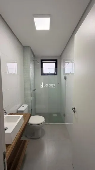 Interior de um banheiro moderno com box de vidro e revestimento branco.