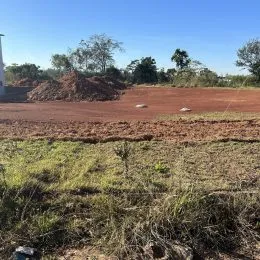 Vista de um terreno aberto com terra vermelha e vegetação seca.