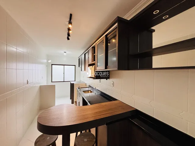 Imagem de uma cozinha com armários escuros e revestimento branco.