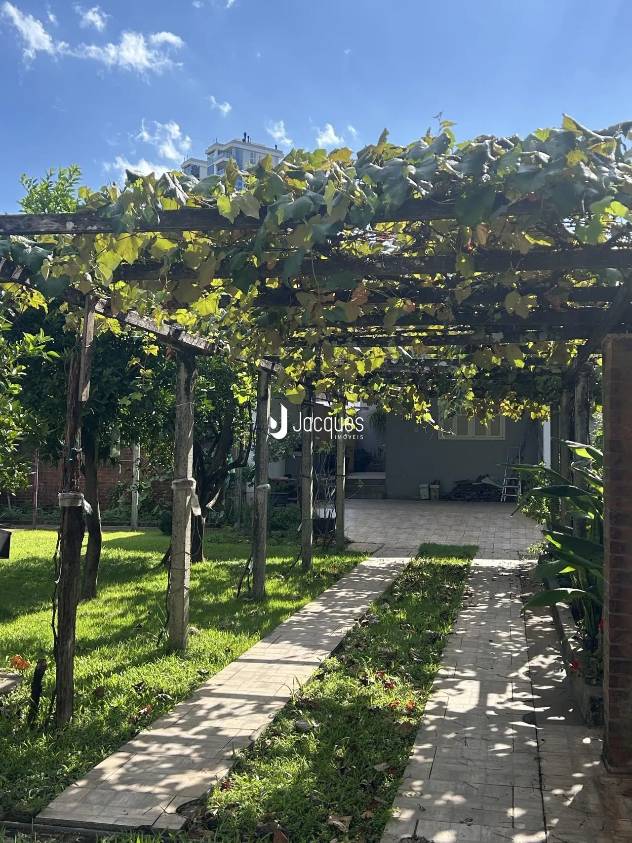 Vista externa de um jardim com pergolado e caminho de pedras.