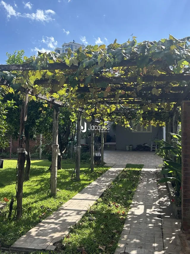 Vista externa de um jardim com pergolado e caminho de pedras.