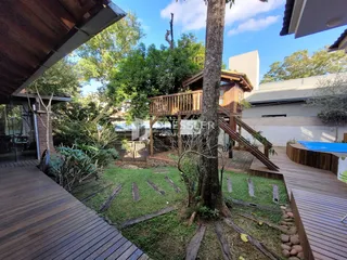 Vista externa de um jardim com deck de madeira e vegetação.