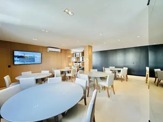 Ambiente de jantar amplo com mesas brancas e cadeiras em um imóvel.