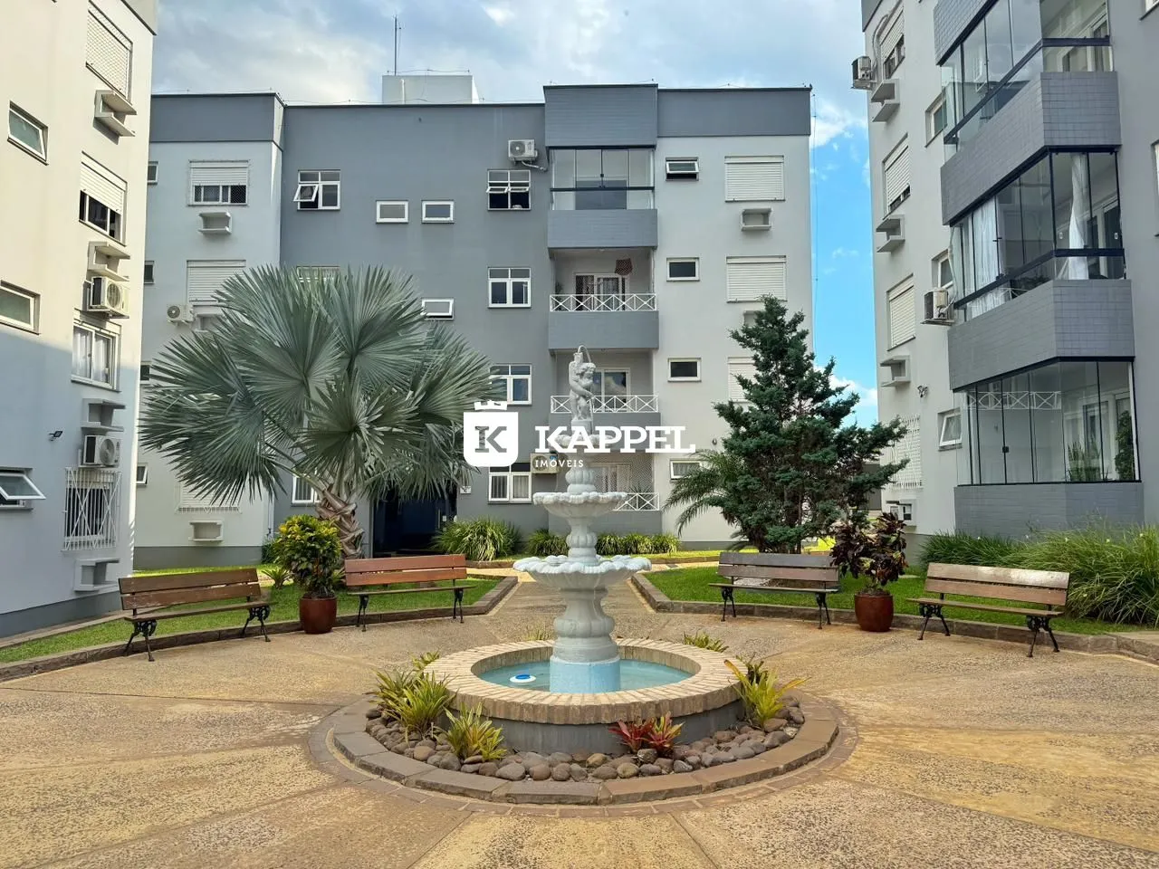 Vista externa de um complexo residencial com jardim central e fonte.