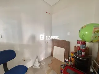 Uma foto interna mostra uma sala com paredes brancas e alguns itens de decoração.