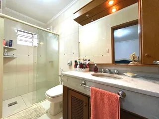 Interior de um banheiro com revestimento cerâmico e box de vidro.