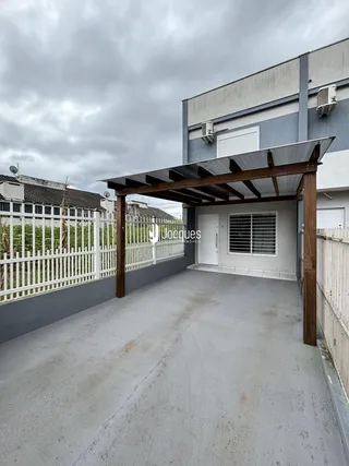 Vista externa de uma área coberta com pérgula e muro branco.