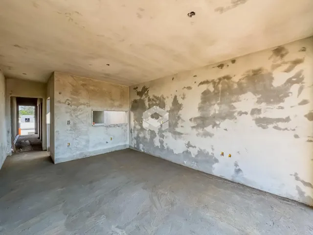 Interior de uma sala com paredes descascadas e piso cru.