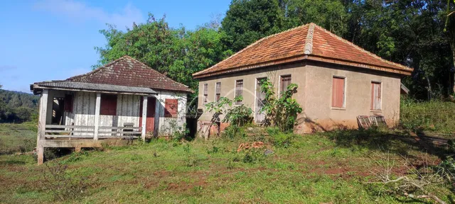 Fachada de uma casa rústica com telhado de telhas vermelhas em uma área rural.