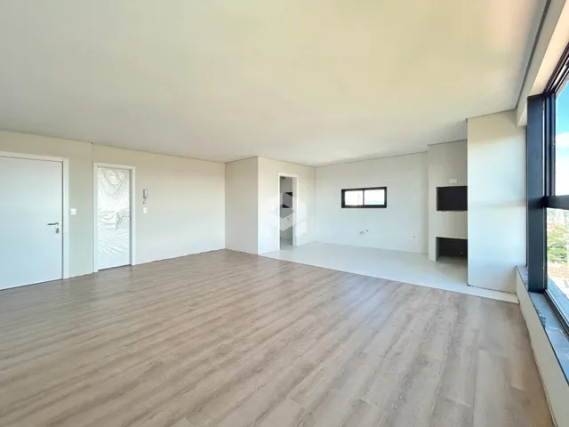 Interior de uma sala ampla com piso de madeira clara e paredes brancas.