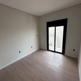 Vista interna de um cômodo com piso de madeira clara e paredes brancas.
