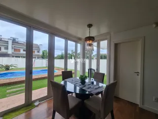 Sala de jantar com vista para o jardim e piscina através de grandes portas de vidro.
