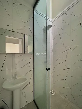 Banheiro com revestimento de mármore nas paredes e box de vidro.