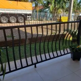 Cerca preta de metal delimitando uma área gramada no exterior da propriedade.