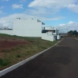 Vista externa de uma residência branca com terreno inclinado e estrada no fundo.