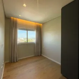 Sala de estar com piso de madeira clara e cortinas claras.