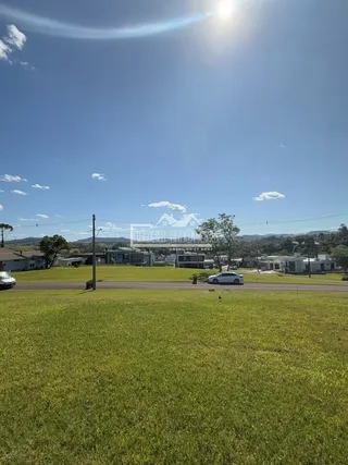 Paisagem de gramado e residências é visível sob um céu azul.