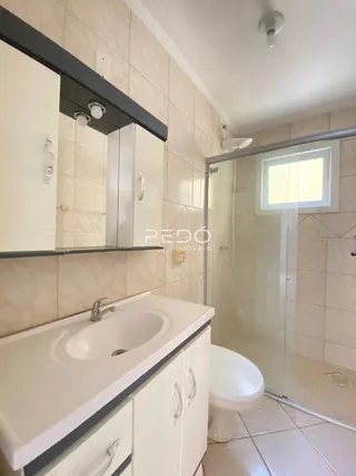 Banheiro com revestimento cerâmico e box de vidro transparente.