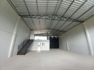 Vista interna de um espaço com estrutura de telhado metálico e paredes brancas.
