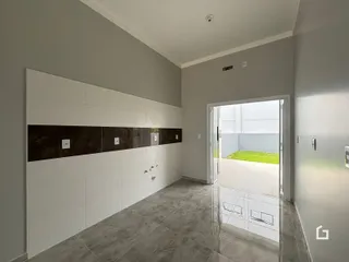 Um corredor interno com paredes brancas e painéis escuros leva a uma área externa.