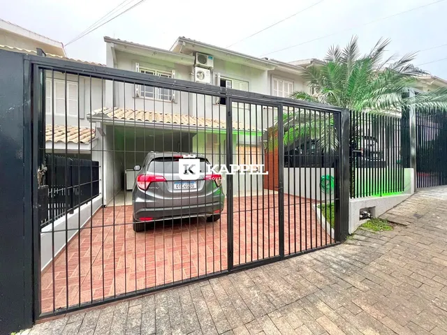 Fachada de uma residência com portão de metal preto e um veículo estacionado no pátio.