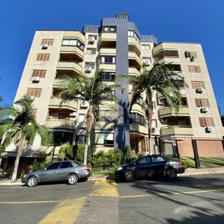 Fachada de um prédio residencial em Lajeado, Brasil, com palmeiras e carros estacionados na rua.