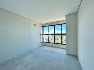 Interior de um cômodo com paredes brancas e piso de concreto cru, com grande janela de vista para a paisagem.