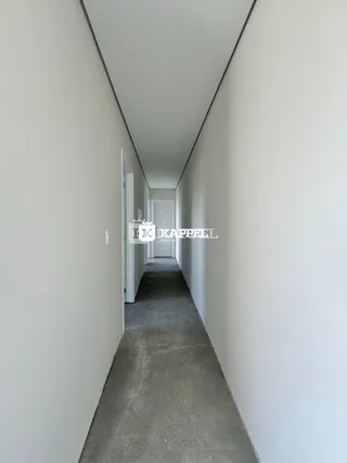 Corredor longo com paredes brancas e piso cinza.