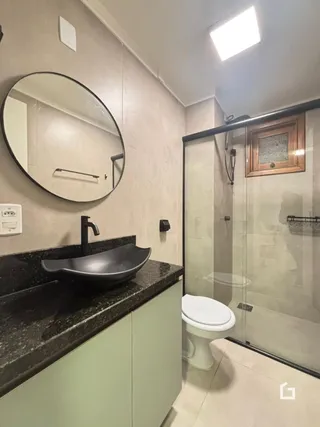 Foto de um banheiro com bancada escura e box de vidro.