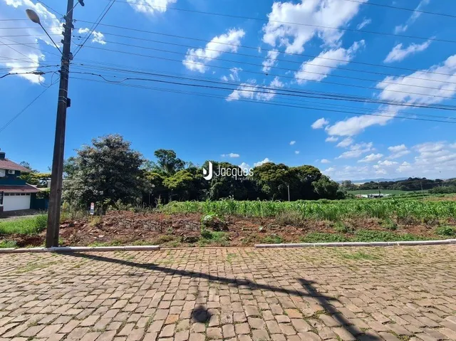 Vista externa de uma área pavimentada com terra e vegetação ao fundo.