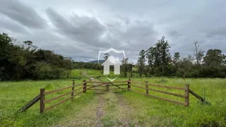 Paisagem de campo com um cercado de madeira e vegetação ao fundo.