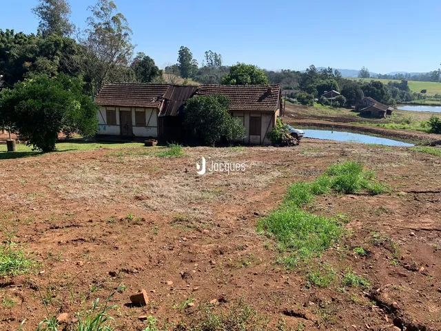 Vista externa de uma casa rural com terreno aberto e vegetação ao redor.