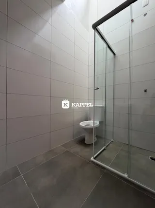 Banheiro com paredes brancas e box de vidro transparente.