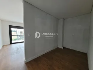 Vista interna de um ambiente com piso de madeira e paredes brancas.