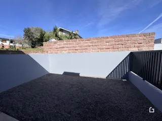 Vista da fachada de uma propriedade com muro de tijolos e área externa.