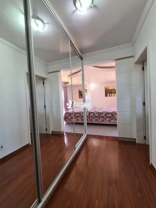 Interior de um quarto com piso de madeira e portas de vidro refletindo o ambiente.