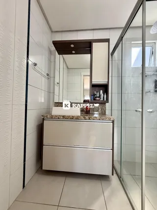 Banheiro com revestimento branco e box de vidro transparente.