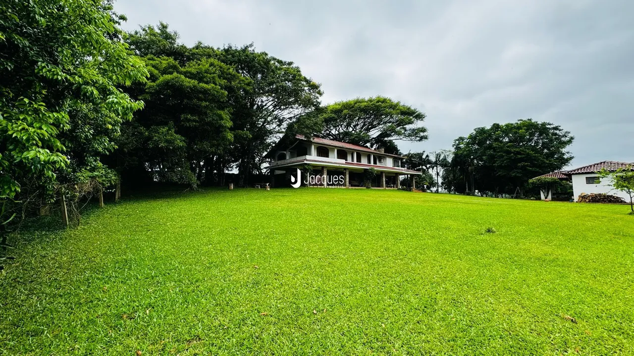Vista externa de uma propriedade com grande gramado e vegetação ao fundo.