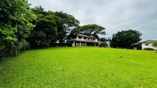 Vista externa de uma propriedade com grande gramado e vegetação ao fundo.