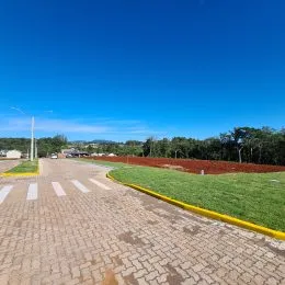 Foto da entrada de uma propriedade com pavimento e gramado sob um céu azul.