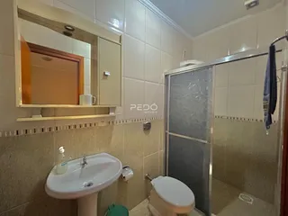 Foto interna de um banheiro com azulejos brancos e box de vidro.