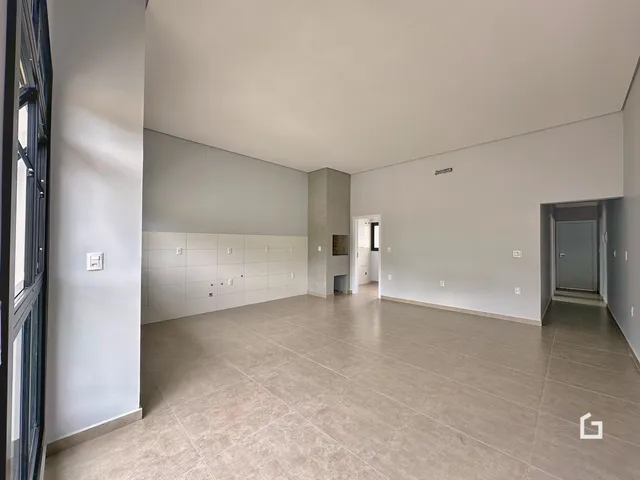 Interior de uma sala ampla com piso de cerâmica clara e paredes brancas.